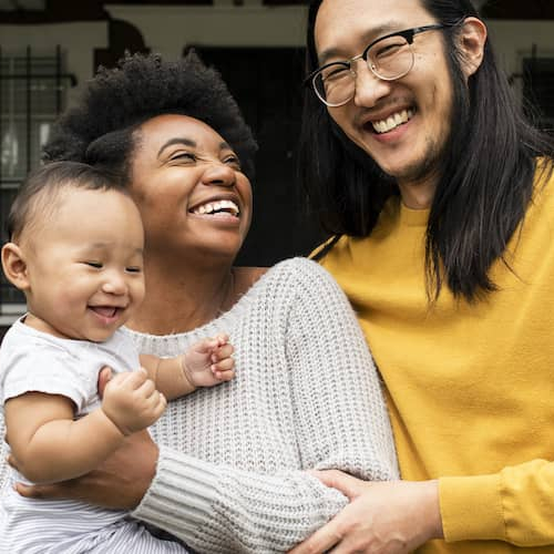 Smiling family with baby in front of new home.