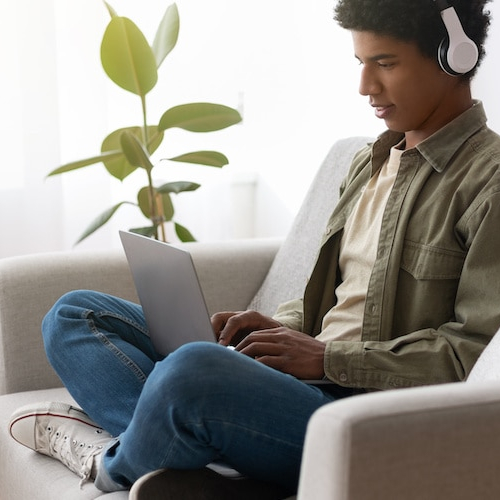 Image of man wearing headphones, staring down at laptop on couch.