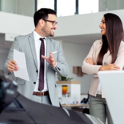 Man in a suit showing a car to a woman and smiling.
