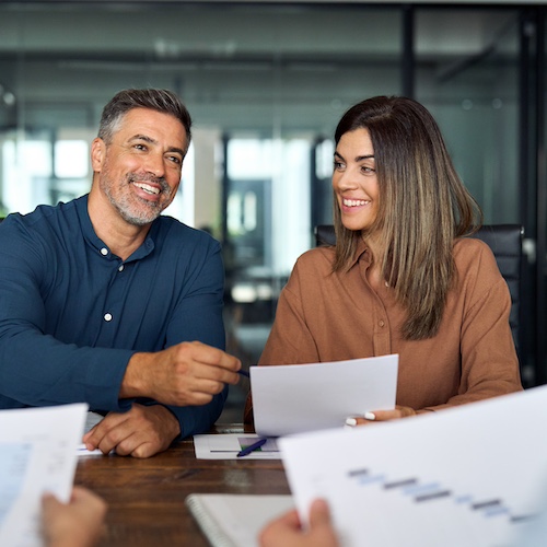 Two people in a group business meeting while holding papers.