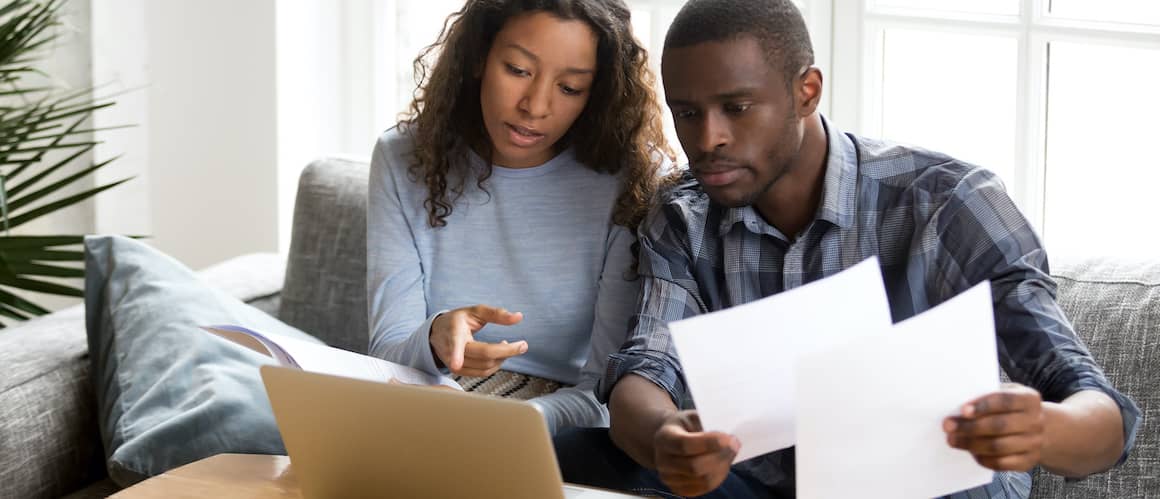 Couple reviewing documents on laptop, possibly home related.