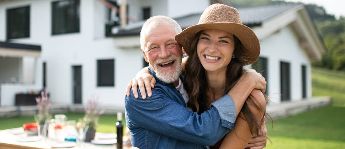 A woman hugging her father in front of a property possibly in woods.